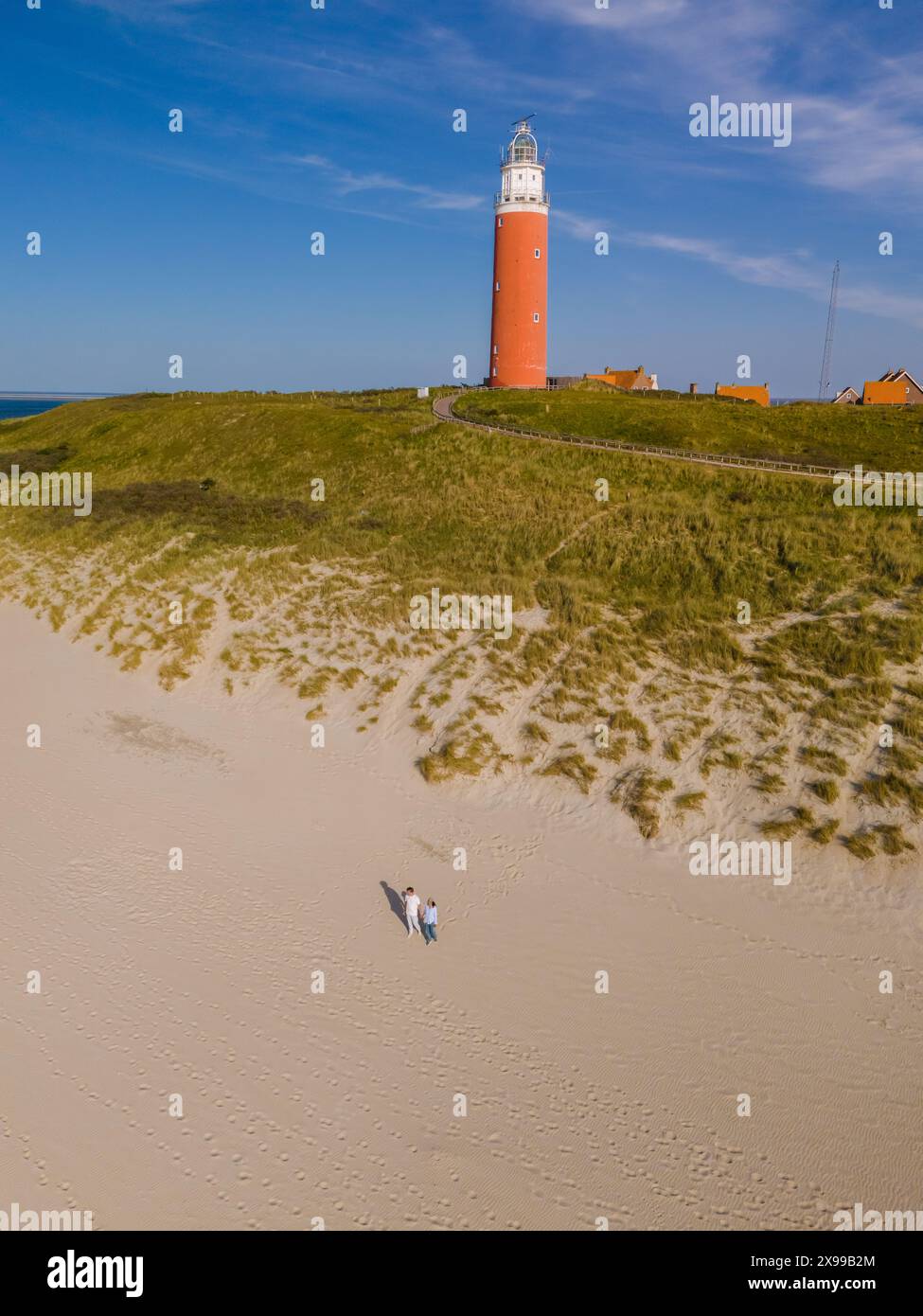 Una vista dall'alto di un faro maestoso che si erge su una spiaggia di sabbia, che getta la sua luce guida sulla vasta distesa della costa di Texel nei Paesi Bassi. Foto Stock Una vista dall'alto di un faro maestoso che si erge su una spiaggia di sabbia, che getta la sua luce guida sulla vasta distesa della costa di Texel nei Paesi Bassi. Foto Stock