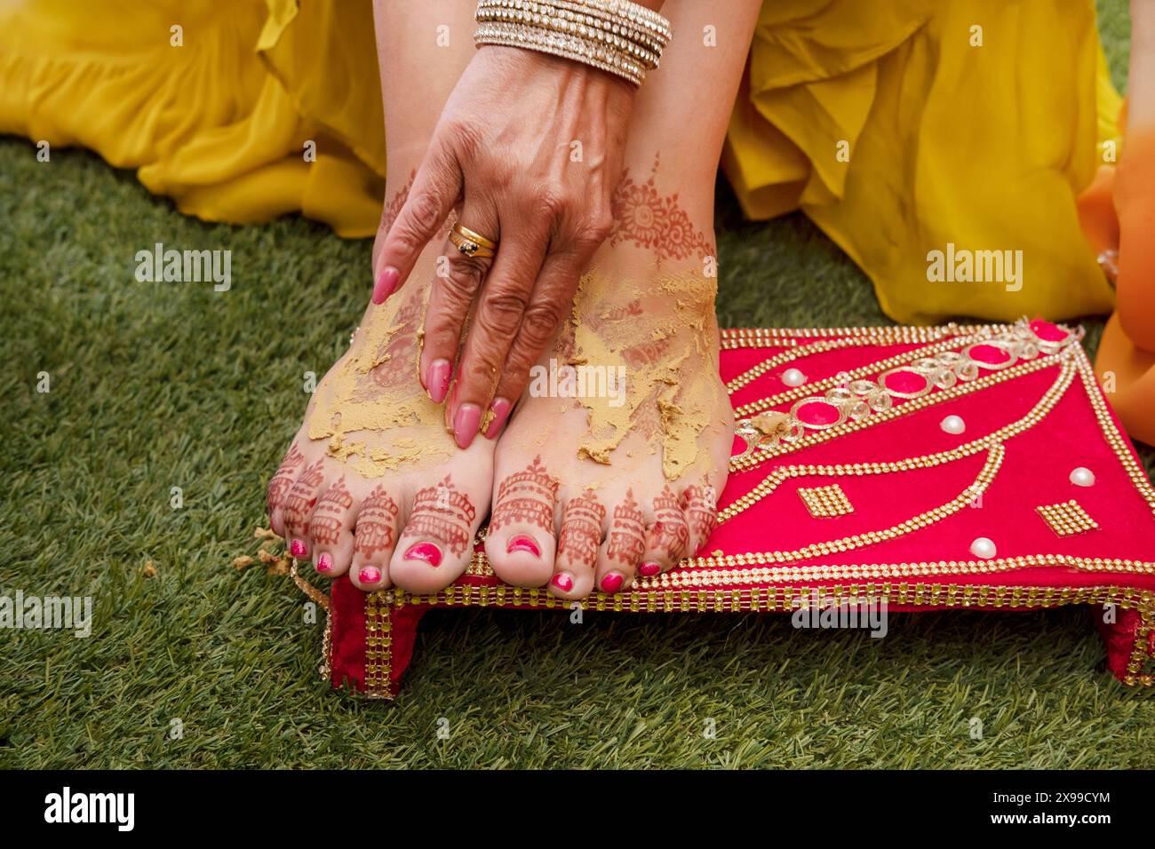 I piedi della sposa adornati da intricati disegni di henné o mehndi sono ricoperti di pasta curcuma parte della cerimonia Haldi in un tradizionale matrimonio indiano Foto Stock