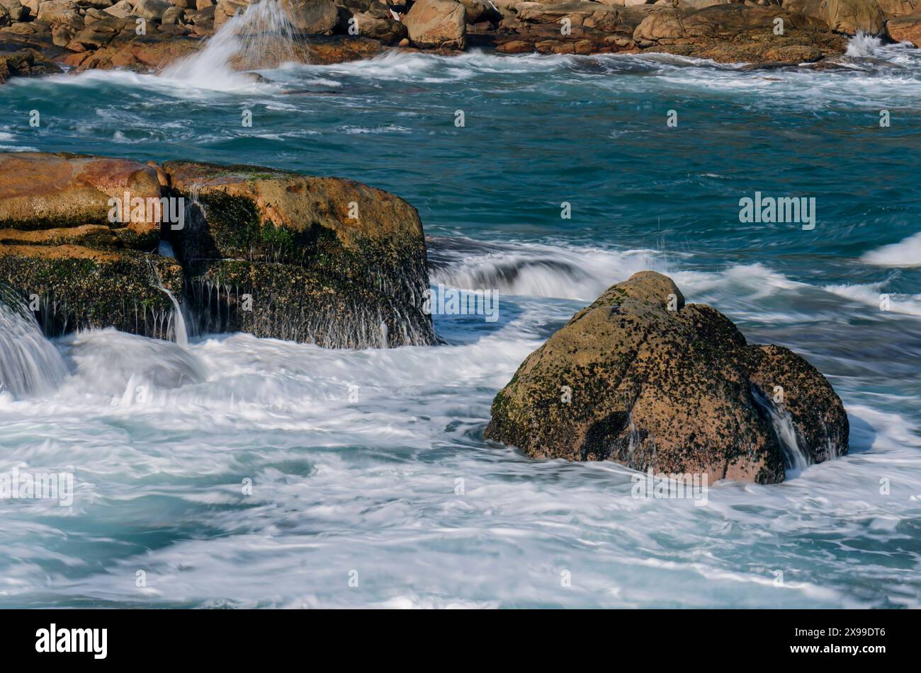 Onde di mare che si infrangono sulle rocce sul lato costiero di una spiaggia a Shek o, l'isola di Hong Kong. Una lunga esposizione. Foto Stock