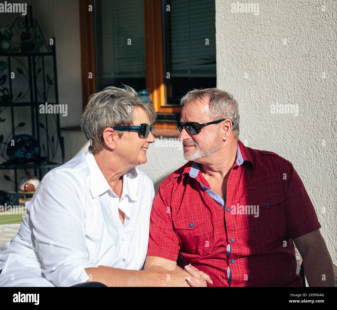 Donna e uomo sorridenti con occhiali da sole che si guardano con affetto sul loro portico Foto Stock