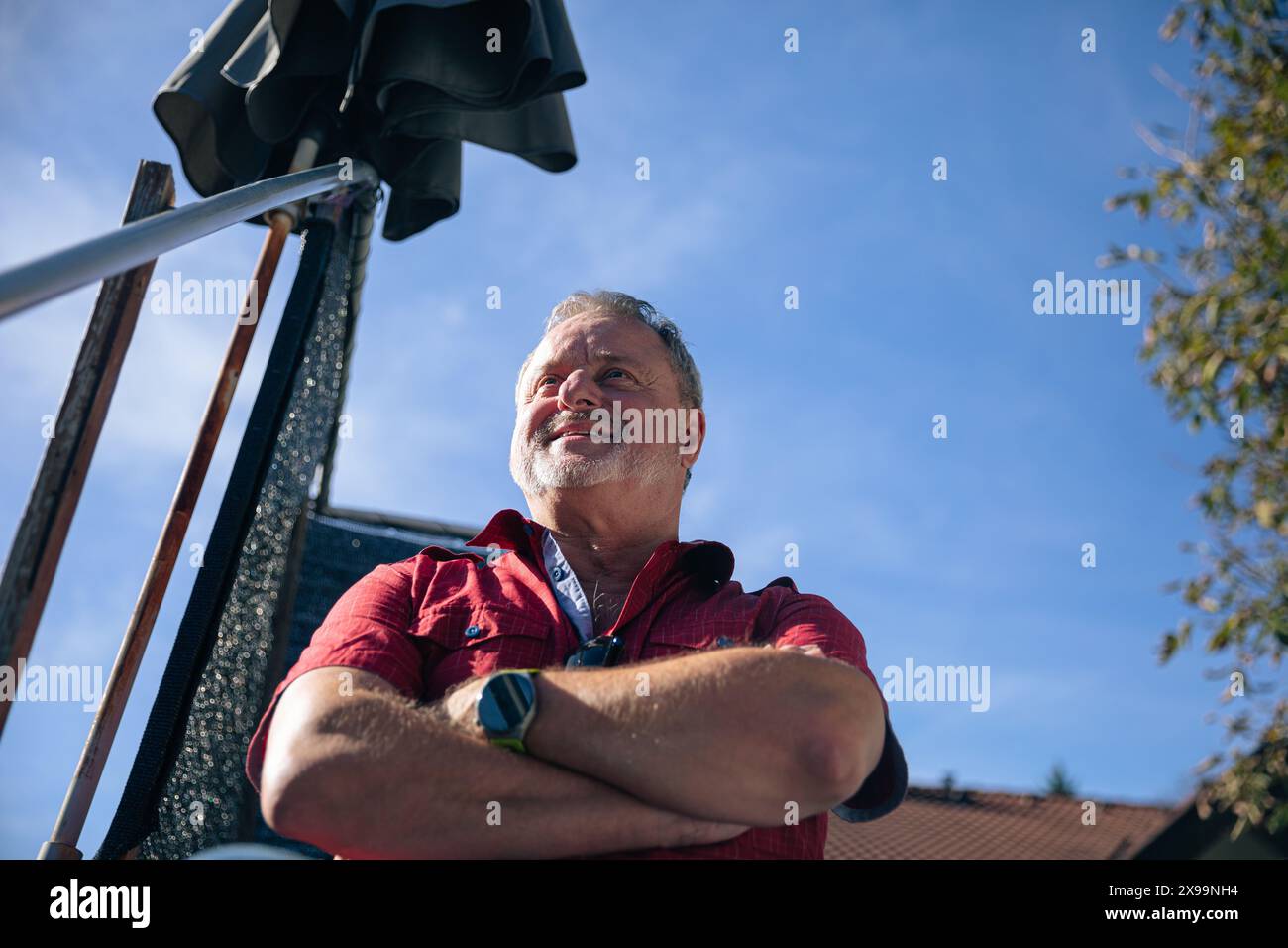Angolo verso l'alto di un anziano attento che guarda verso il cielo, braccia incrociate in una posa di riflessione Foto Stock