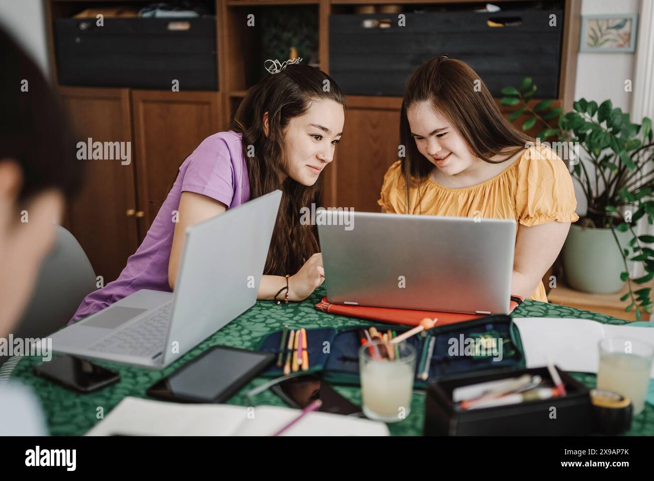 Donna sorridente che condivide il laptop con la sorella affetta da sindrome di Down a casa Foto Stock