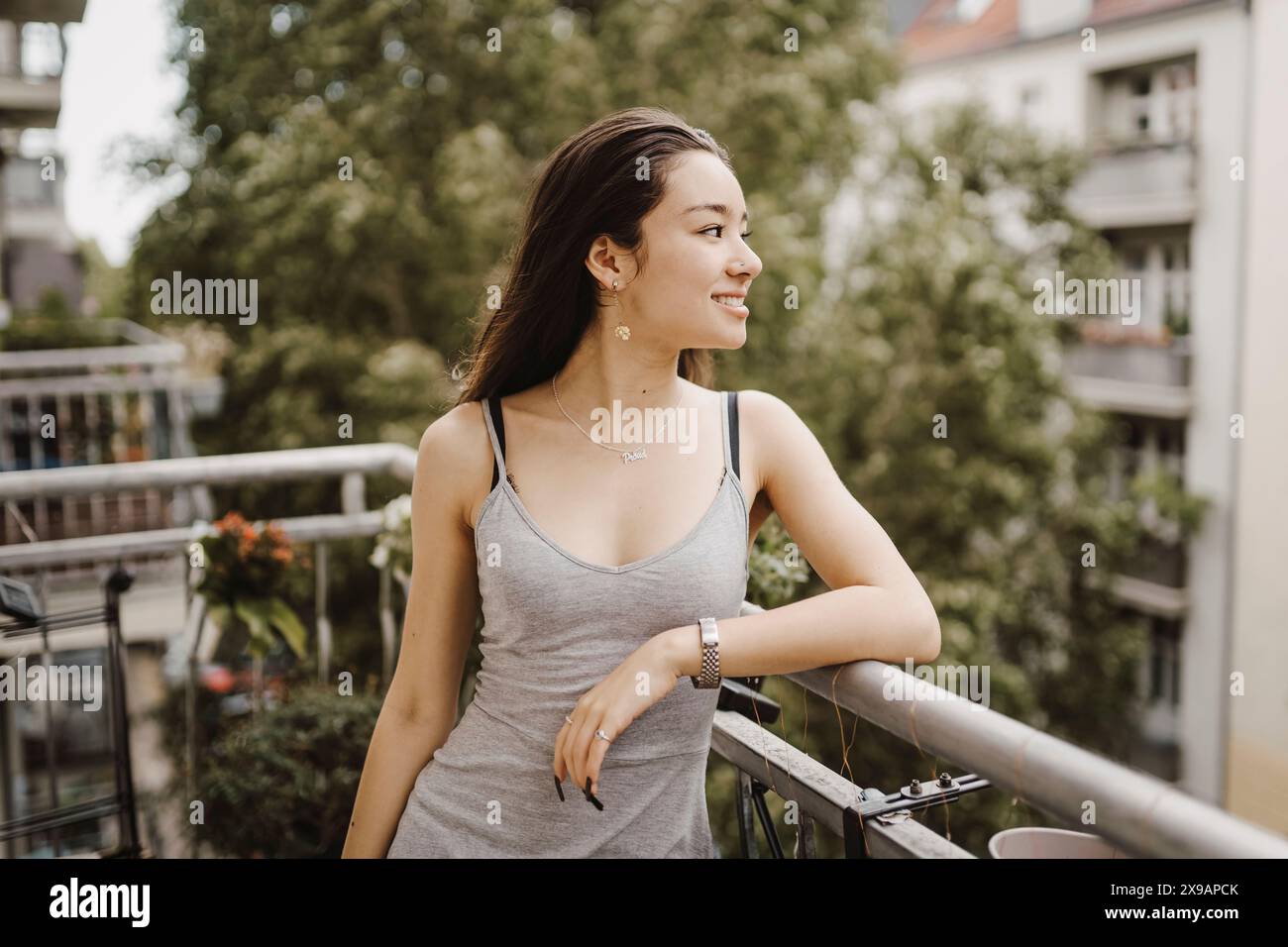 Donna sorridente che guarda via mentre si appoggia sulla ringhiera in balcone Foto Stock