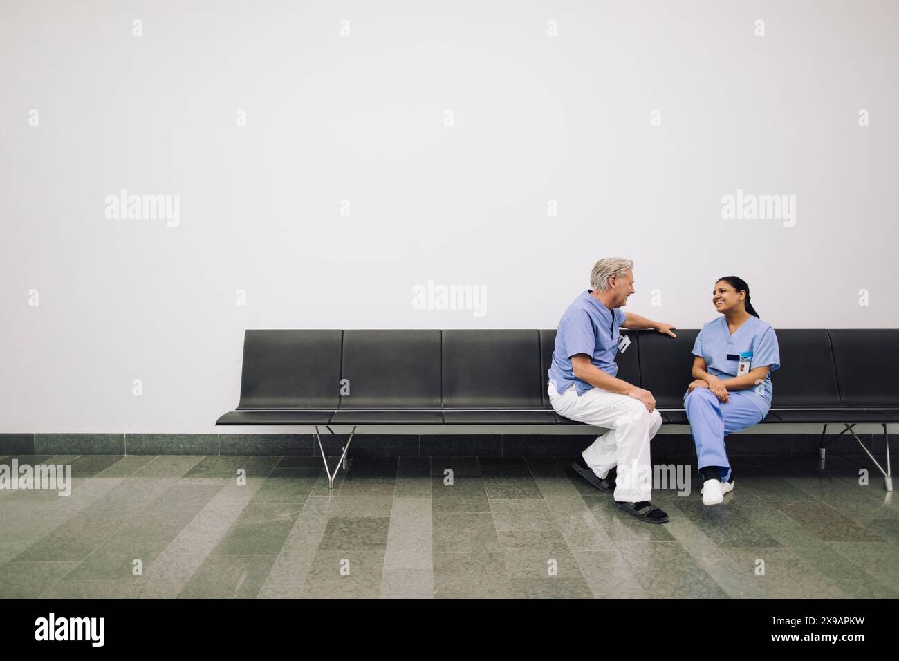 Intera lunghezza di medici maschili e femminili discutere mentre seduto sulla panchina in ospedale Foto Stock