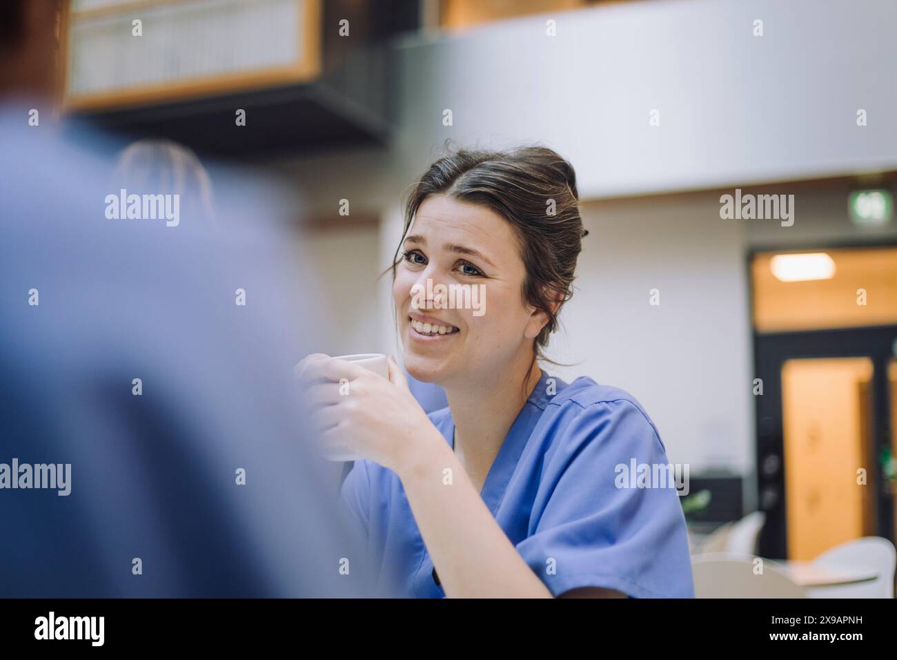 Medico donna sorridente con collega in mensa all'ospedale Foto Stock