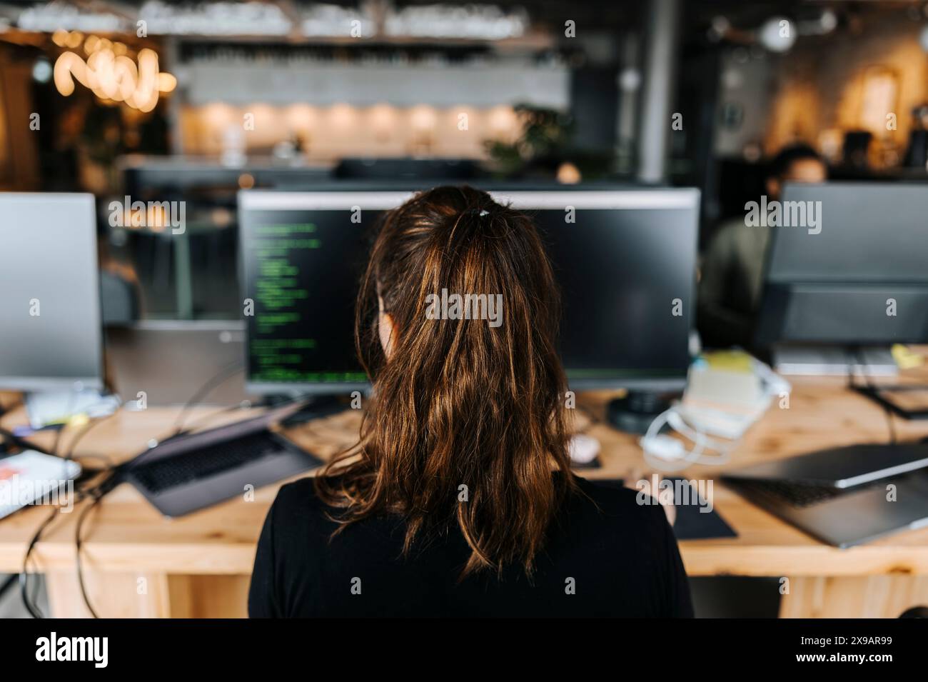 Parte posteriore del codificatore femminile con coda di cavallo seduta alla scrivania in ufficio Foto Stock