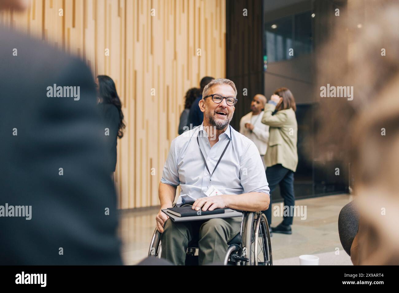 Uomo d'affari maturo con disabilità seduto su sedia a rotelle mentre parla con i partecipanti al centro convegni Foto Stock