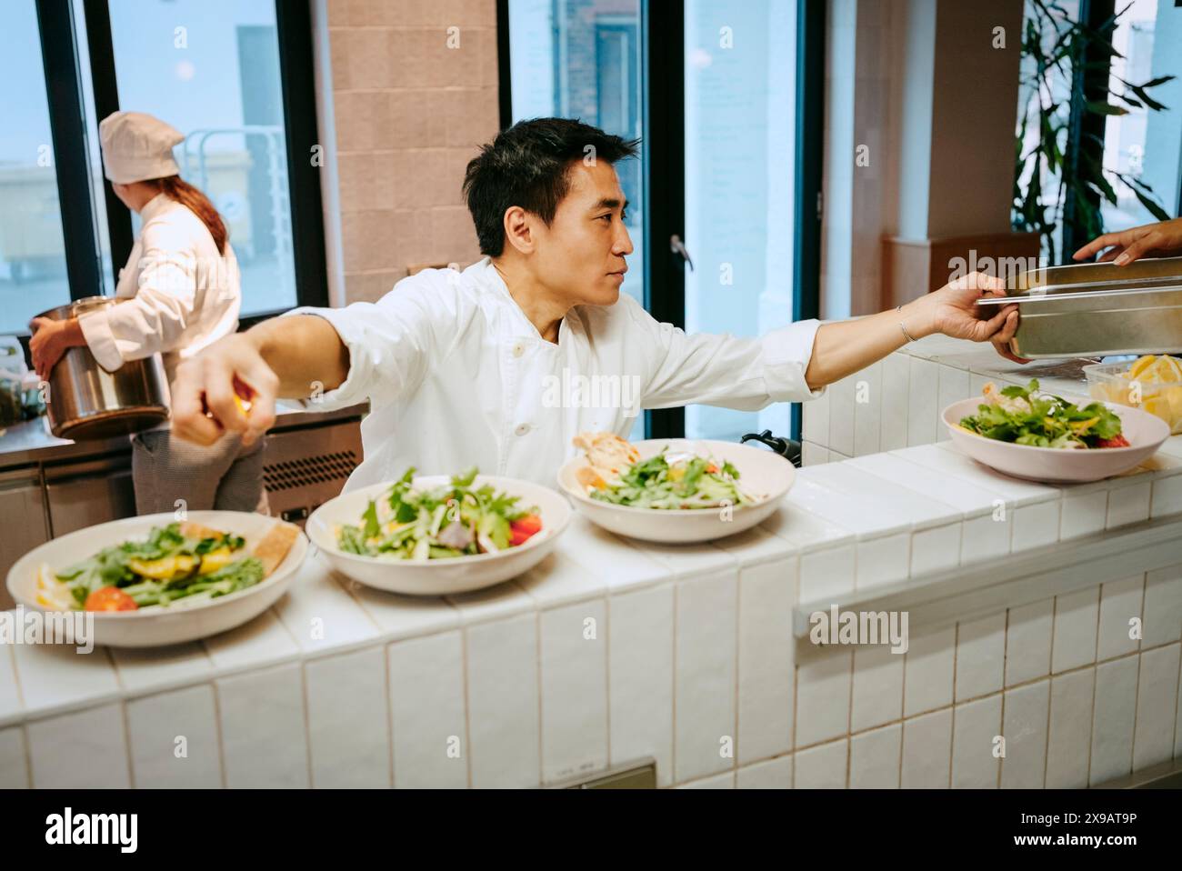 Chef maschile che lavora in multitasking con i colleghi nella cucina commerciale Foto Stock