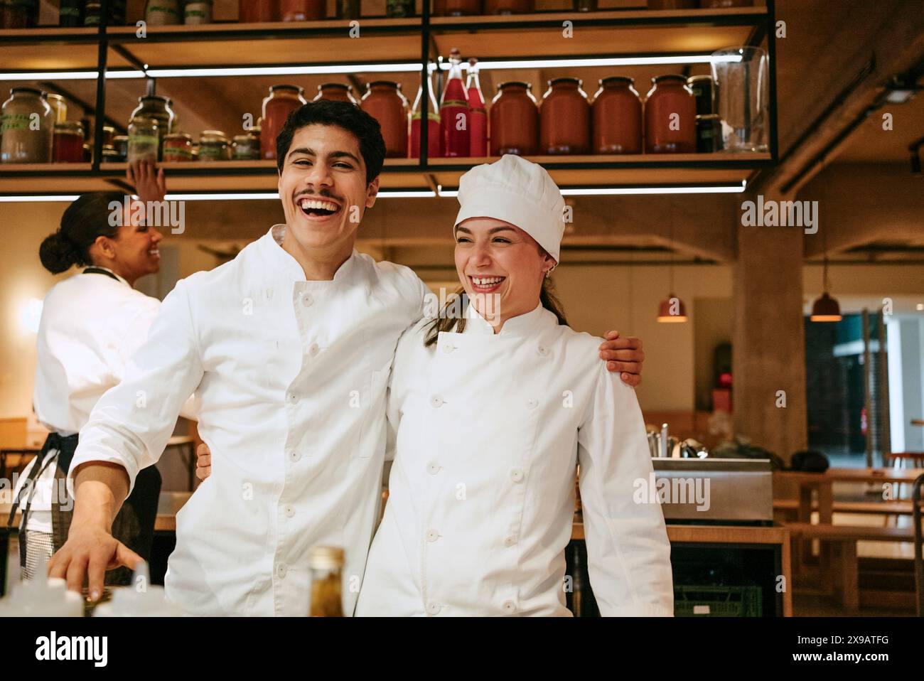 Felice chef maschile con un braccio intorno a una chef donna che si diverte mentre si trova in una cucina commerciale Foto Stock