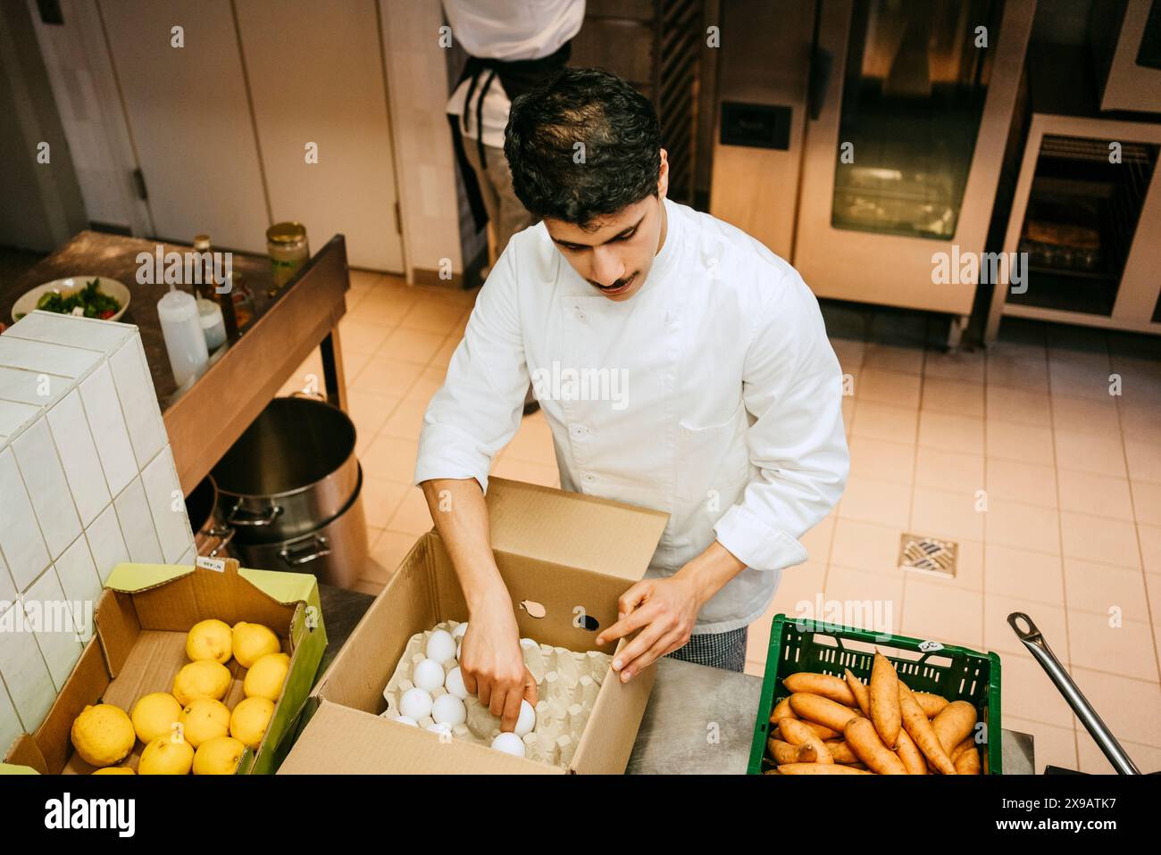 Vista ad angolo alto dello chef maschio che rimuove l'uovo dalla cassa mentre si trova in una cucina commerciale Foto Stock