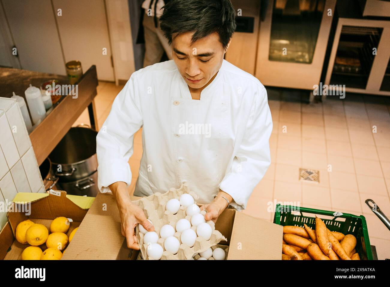 Vista ad angolo alto dello chef maschio che rimuove la cassa dell'uovo dalla scatola mentre si trova in una cucina commerciale Foto Stock