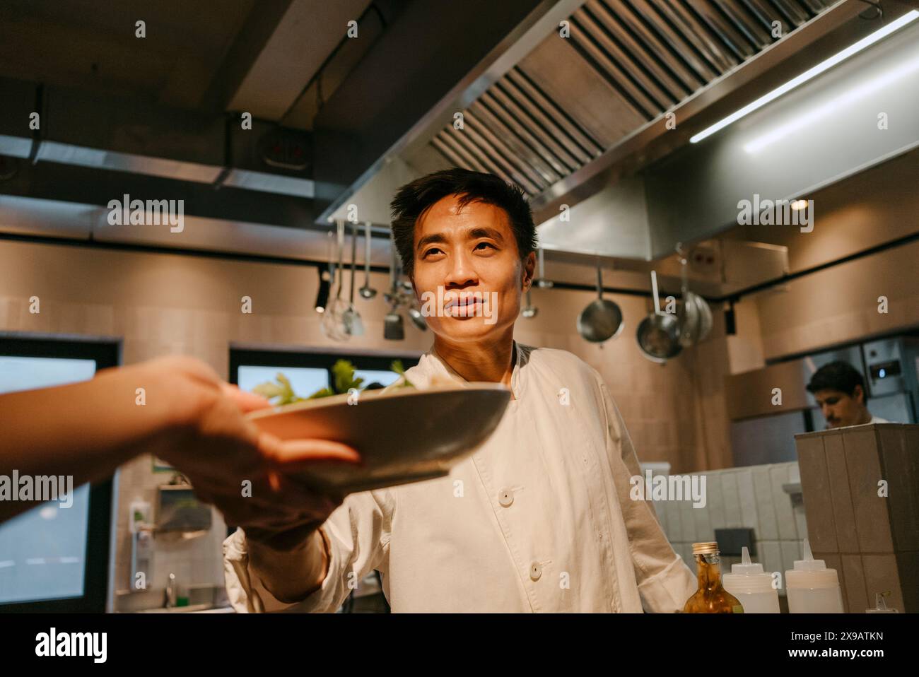 Chef maschile che passa la ciotola per insalate al collega che lavora in cucina commerciale Foto Stock