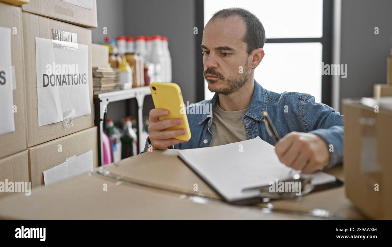 Uomo ispanico con barba controlla il telefono nel magazzino del centro donazioni Foto Stock