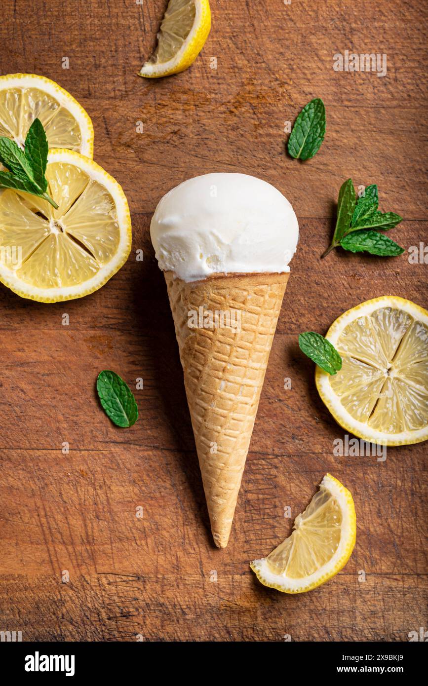 Tazza di gelato al limone con cono di cialda e fette di limone su sfondo di legno, vista dall'alto. Gelato vegano al limone al cocco fatto in casa. Foto Stock