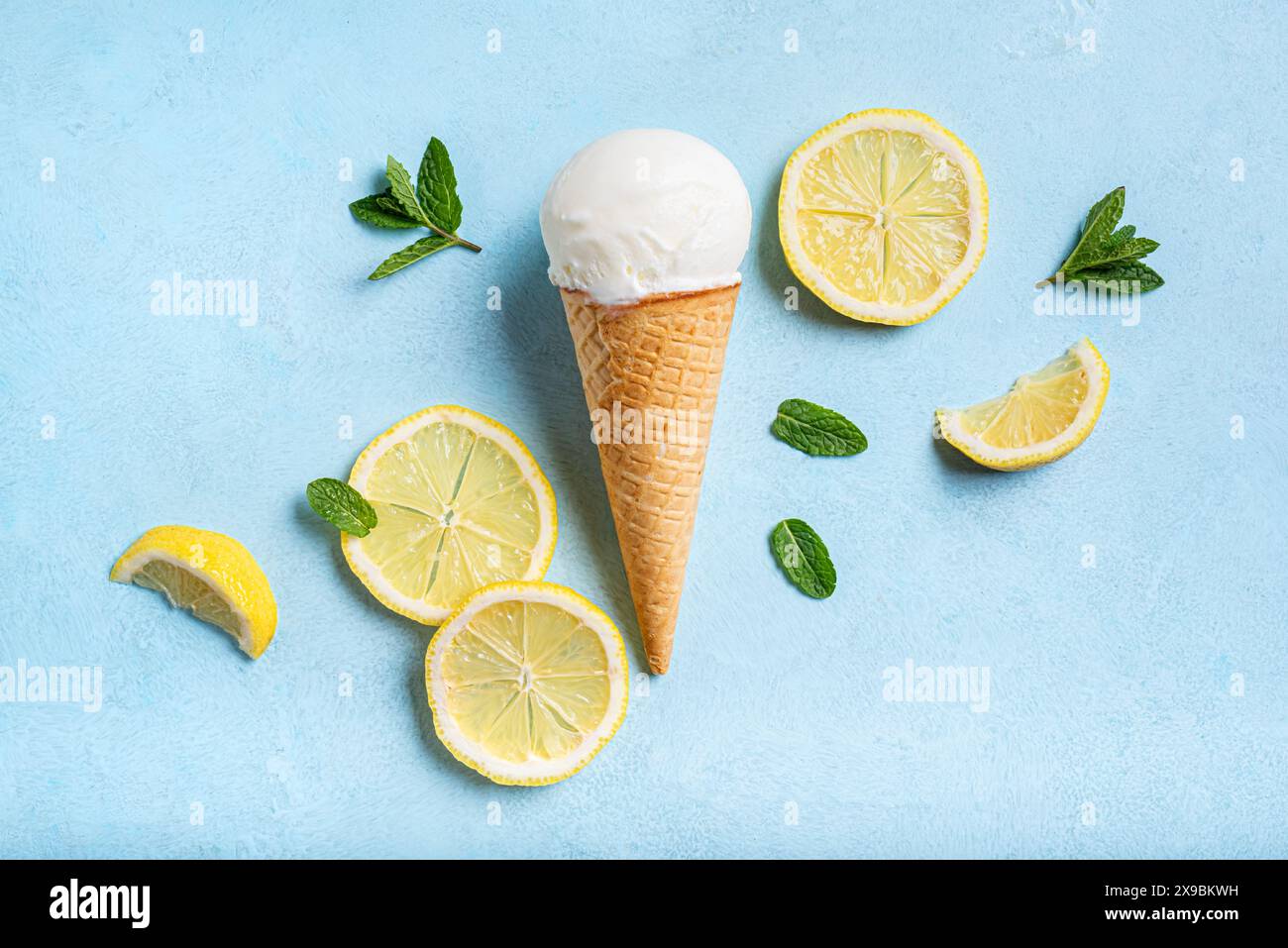 Cucchiaio di gelato al limone con cono di cialda e fette di limone su sfondo azzurro, vista dall'alto. Composizione creativa alla moda. Foto Stock