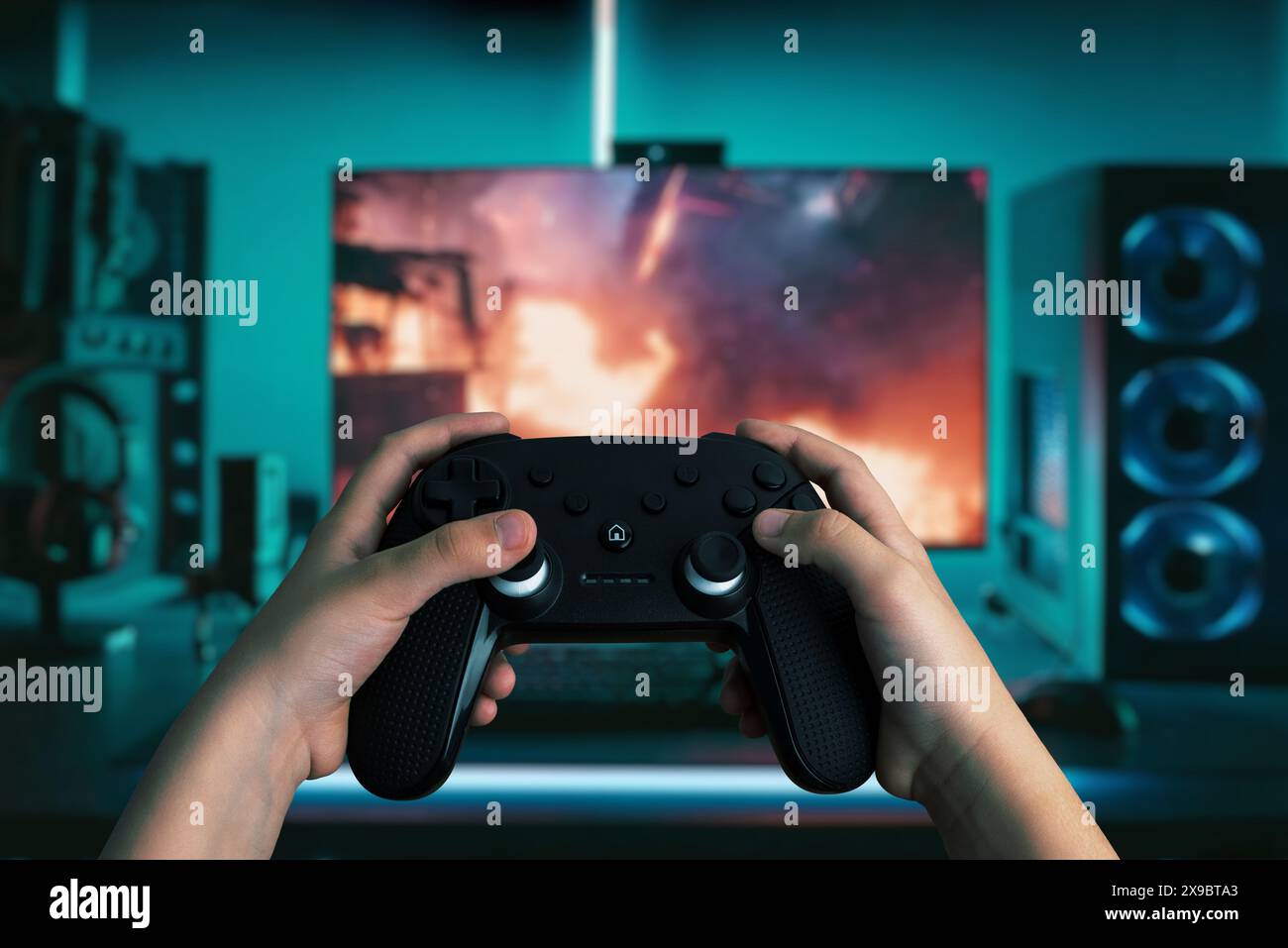 Immagine dinamica delle mani che tengono un gamepad davanti a un moderno computer per videogame, con luci LED vibranti, per giocare a un gioco ricco di azione Foto Stock