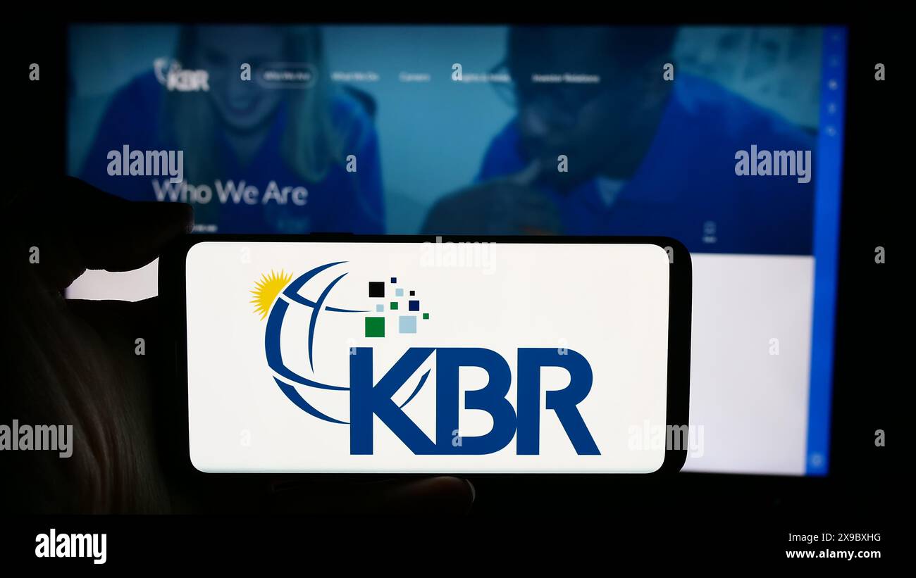 Persona che detiene un cellulare con il logo della società di ingegneria e costruzione statunitense KBR Inc. Di fronte alla pagina Web aziendale. Mettere a fuoco il display del telefono. Foto Stock