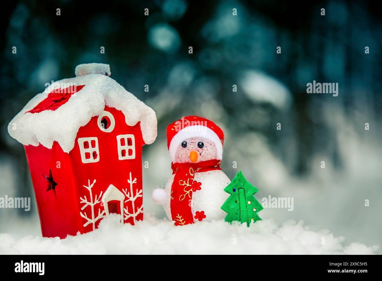 Una scena invernale festosa con una casa rossa e un pupazzo di neve in un ambiente innevato con un piccolo albero Foto Stock