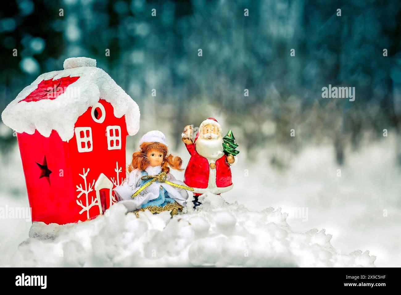 Scena natalizia con la statuetta di Babbo Natale, una bambola e una casa rossa ricoperta di neve Foto Stock