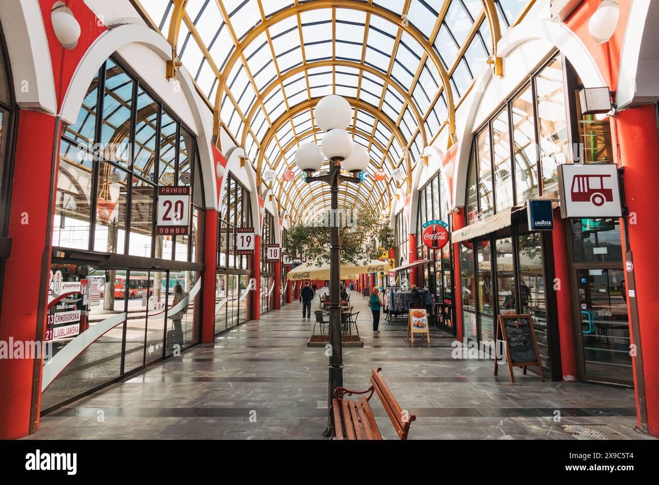 Una stazione degli autobus vuota a Maribor, Slovenia, con colonne rosse, tetto in vetro e negozi su entrambi i lati. Foto Stock