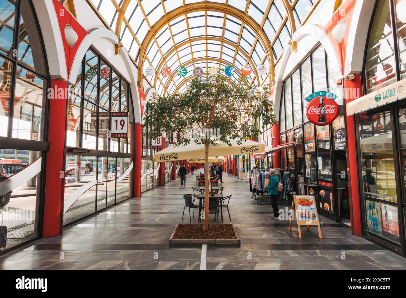 Una stazione degli autobus vuota a Maribor, Slovenia, con colonne rosse, tetto in vetro e negozi su entrambi i lati. Foto Stock