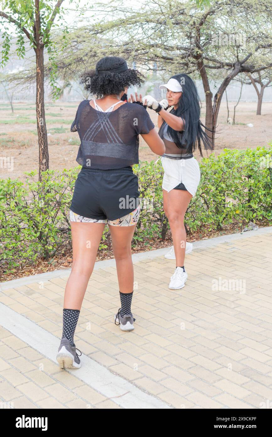 Due donne che praticano tecniche di autodifesa in un parco all'aperto, concentrandosi su manovre di blocco e colpi durante la sessione di fitness. Foto Stock