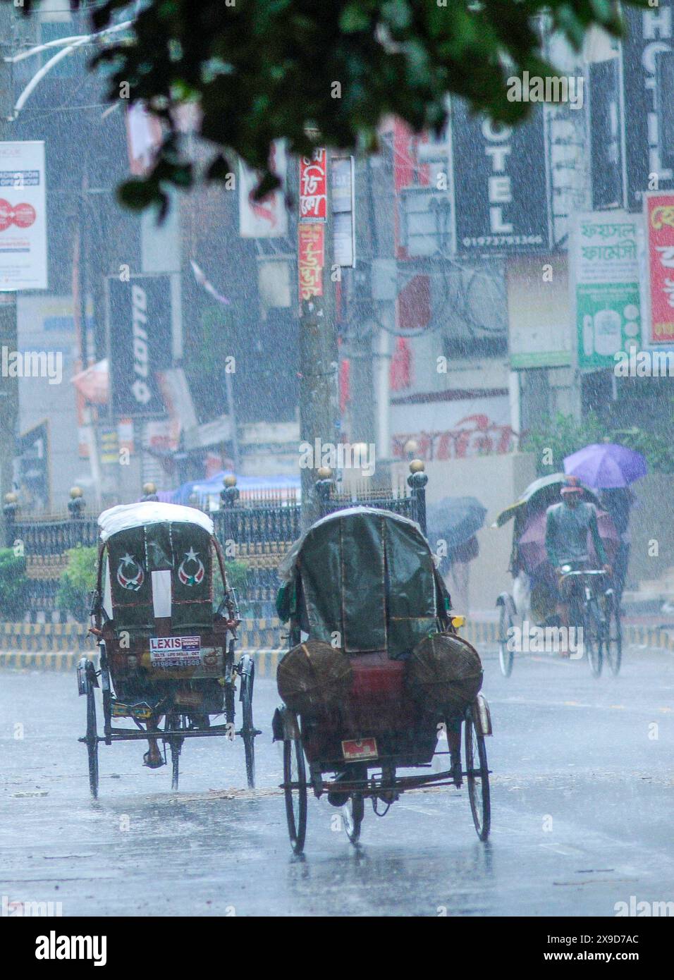 Pedoni che navigano attraverso le strade allagate di Sylhet a causa del ciclone Remal. Negli ultimi giorni, in tutto il paese, sono prevalse forti piogge e le zone costiere hanno subito ingenti danni. Sylhet, Bangladesh. Foto Stock