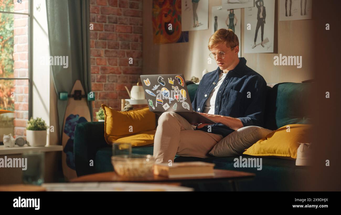 Ritratto di un bell'uomo seduto sul divano, che utilizza un computer portatile nell'elegante appartamento Loft il giorno della soleggiata. Creative male Focused, lavorando su Online Project, pensando ai risultati futuri. Foto Stock