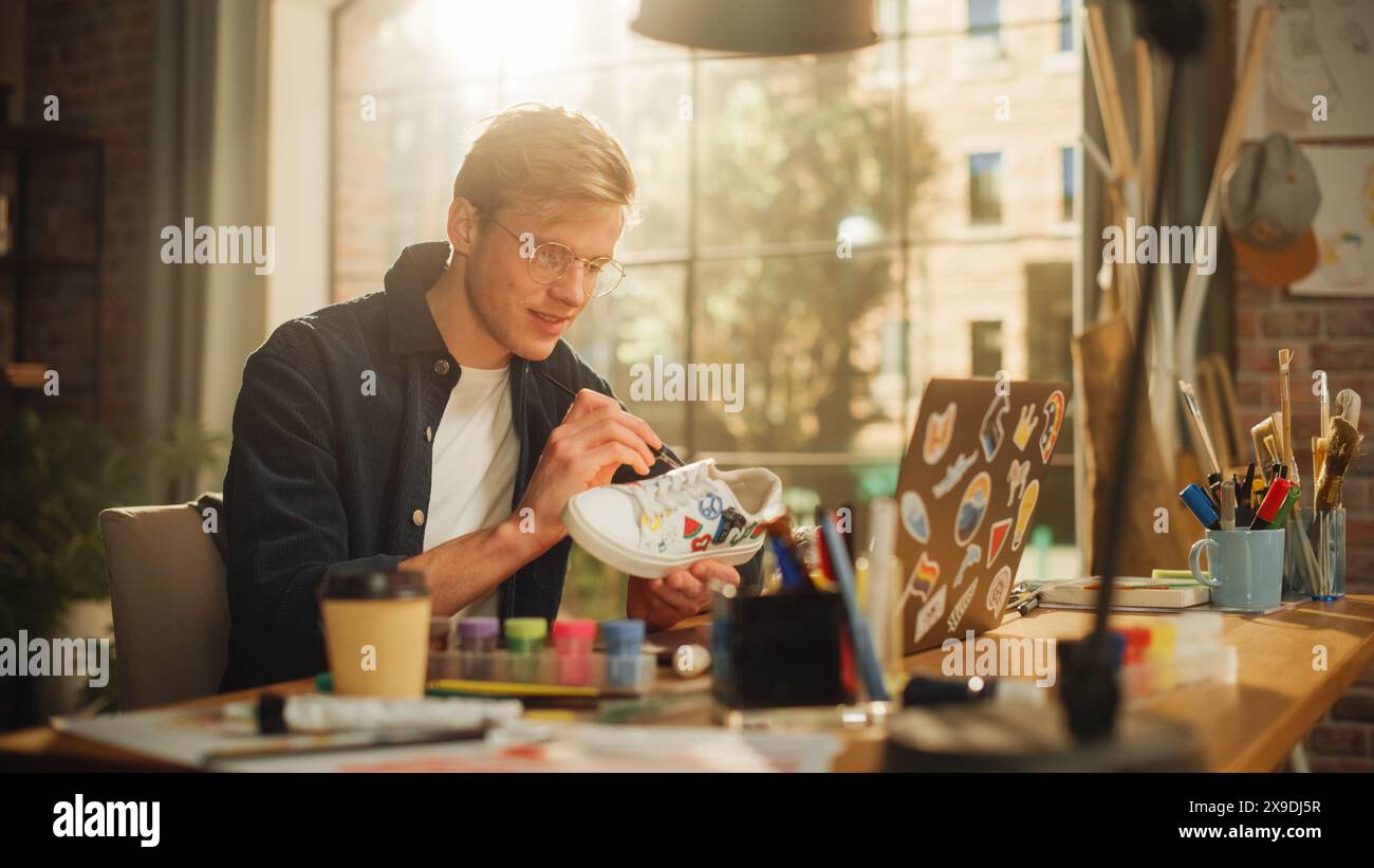 Stilista di moda maschile che crea un nuovo design per un paio di sneakers usate sul suo posto di lavoro. L'artista adolescente si è concentrato sul suo lavoro. Abbigliamento alla moda personalizzato ed ecologico. Foto Stock