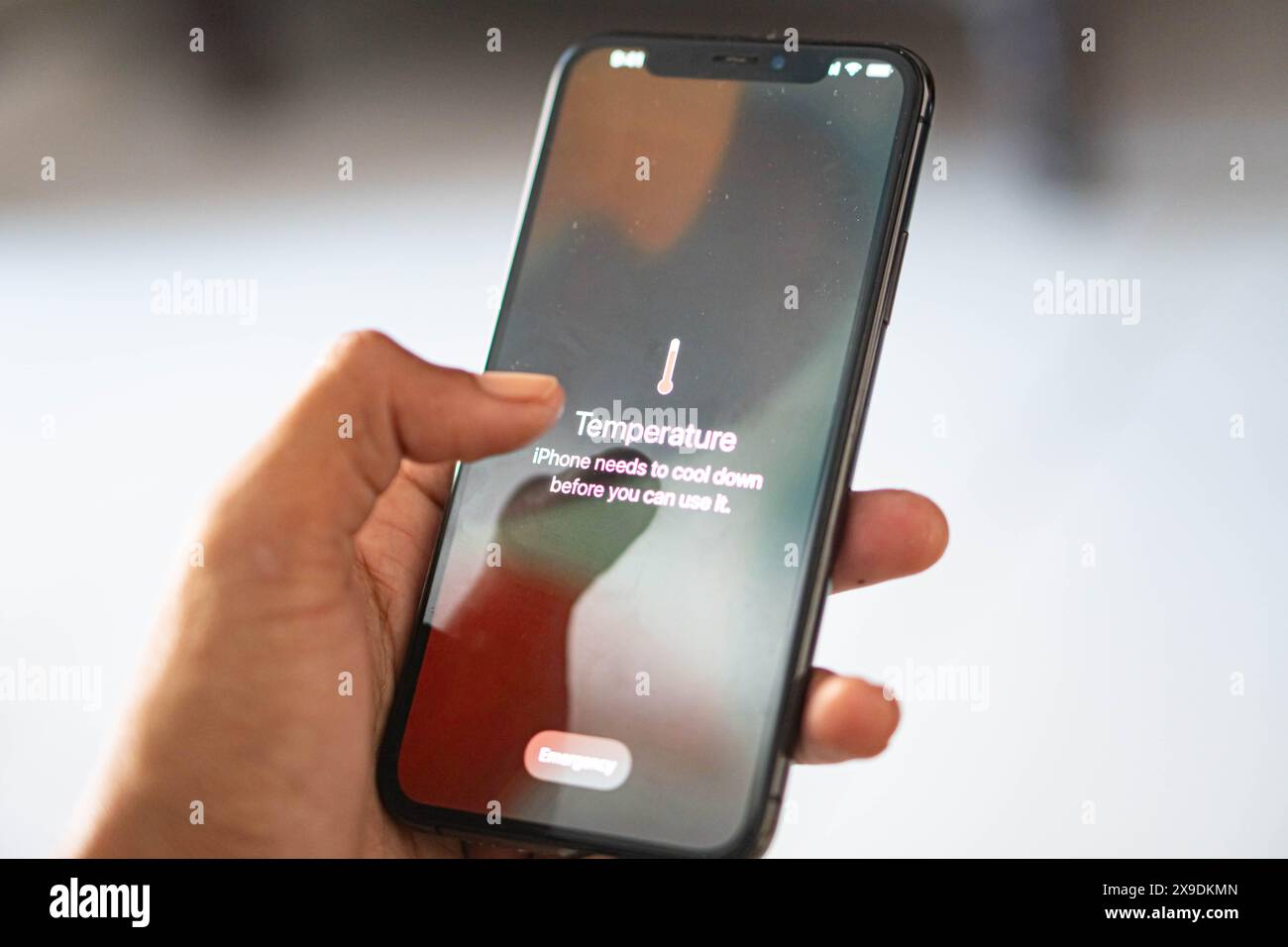 Una mano che tiene premuto uno smartphone e visualizza un messaggio di avviso relativo alla temperatura, che indica che il dispositivo deve raffreddarsi prima dell'uso. Foto Stock