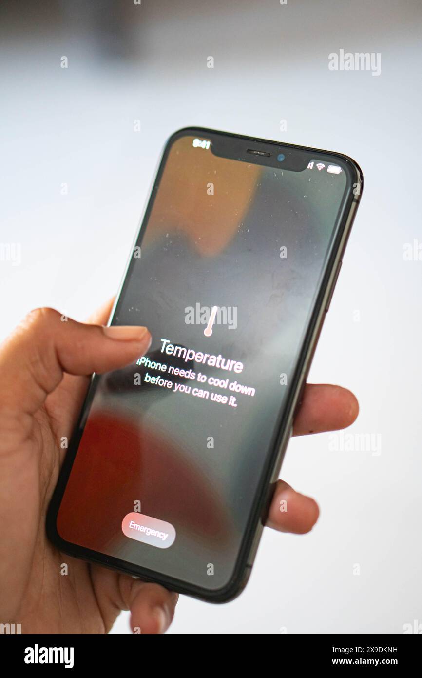 Una mano che tiene premuto uno smartphone e visualizza un messaggio di avviso relativo alla temperatura che indica che l'iPhone deve raffreddarsi prima di poterlo utilizzare. Foto Stock