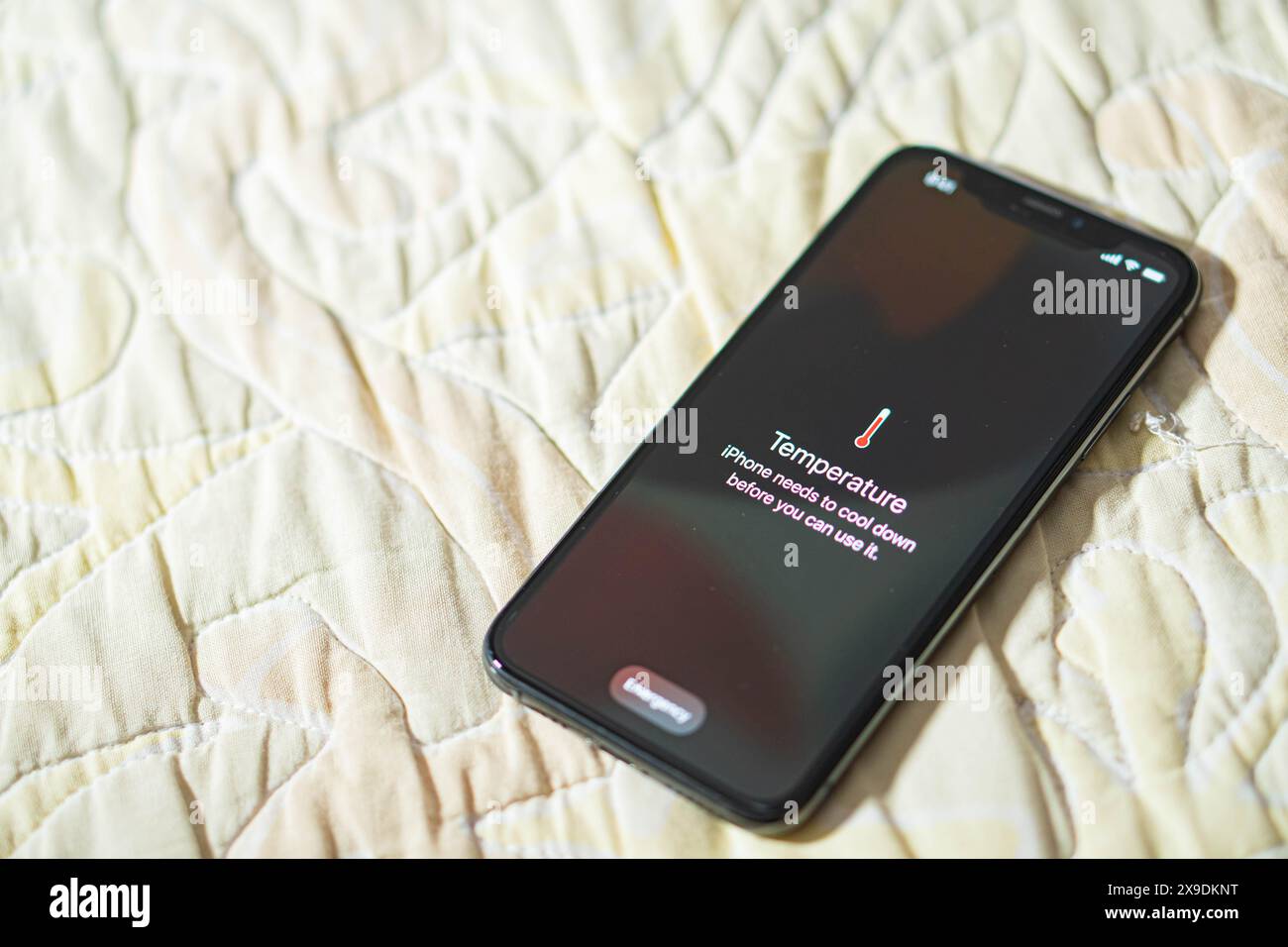 Uno smartphone che visualizza un messaggio di avviso relativo alla temperatura, per indicare che deve raffreddarsi prima dell'uso. Il telefono è posizionato su una superficie in tessuto trapuntato. Foto Stock