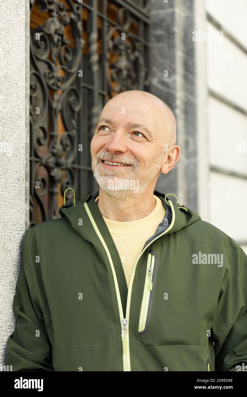 Uomo calvo maturo sorridente con la giacca di marmotta verde di un cancello di ferro decorato Foto Stock