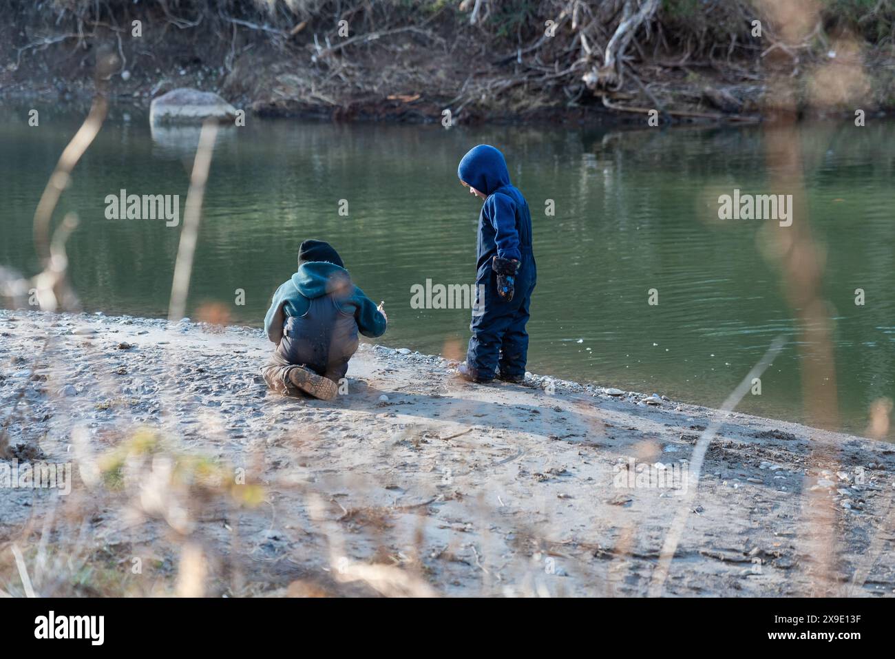 Due bambini in abiti invernali esplorano in riva al fiume Foto Stock