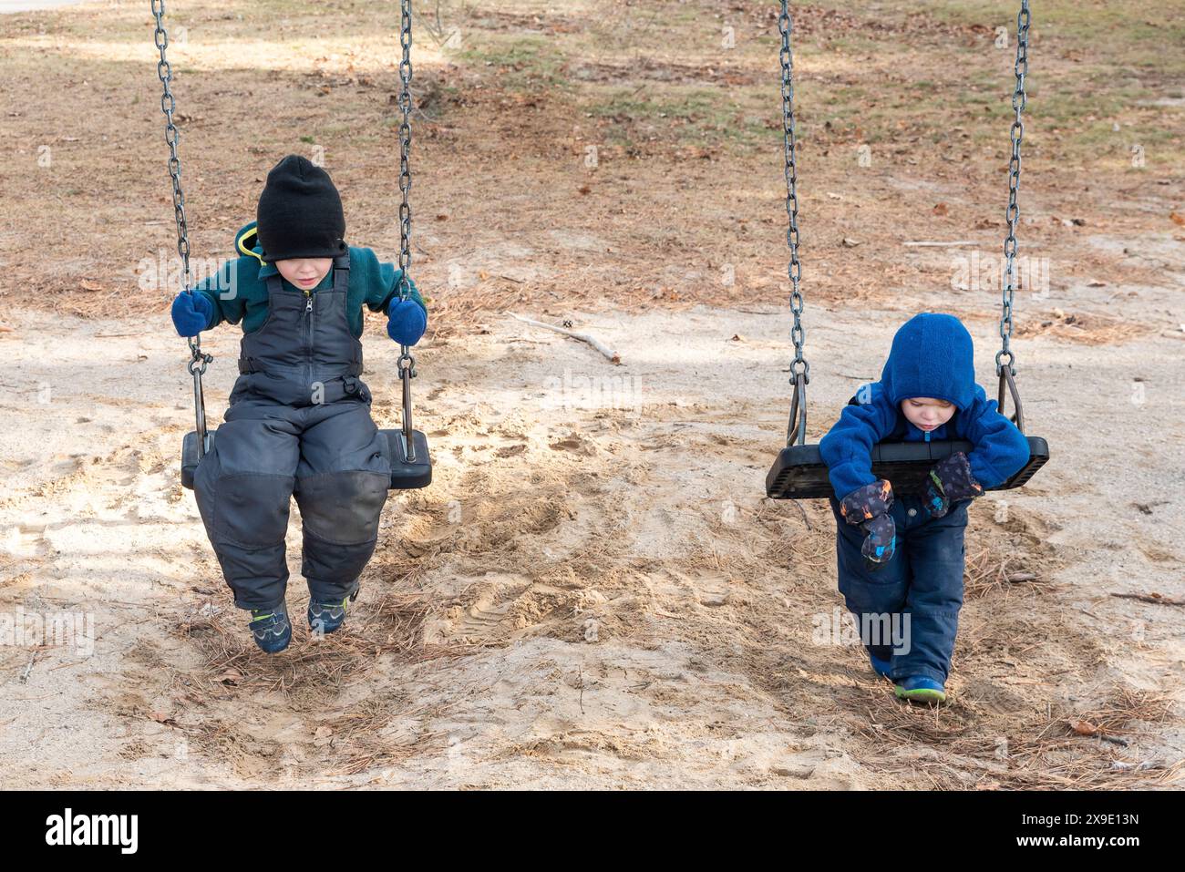 Bambini con abbigliamento invernale che giocano sulle altalene nel parco giochi Foto Stock