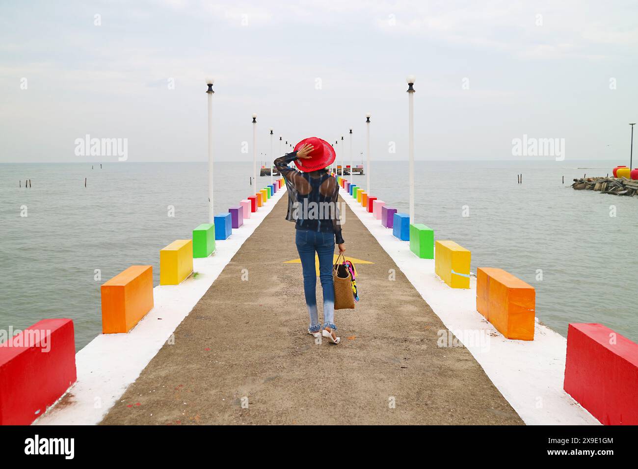 Donna con cappello rosso che cammina sul molo colorato Foto Stock