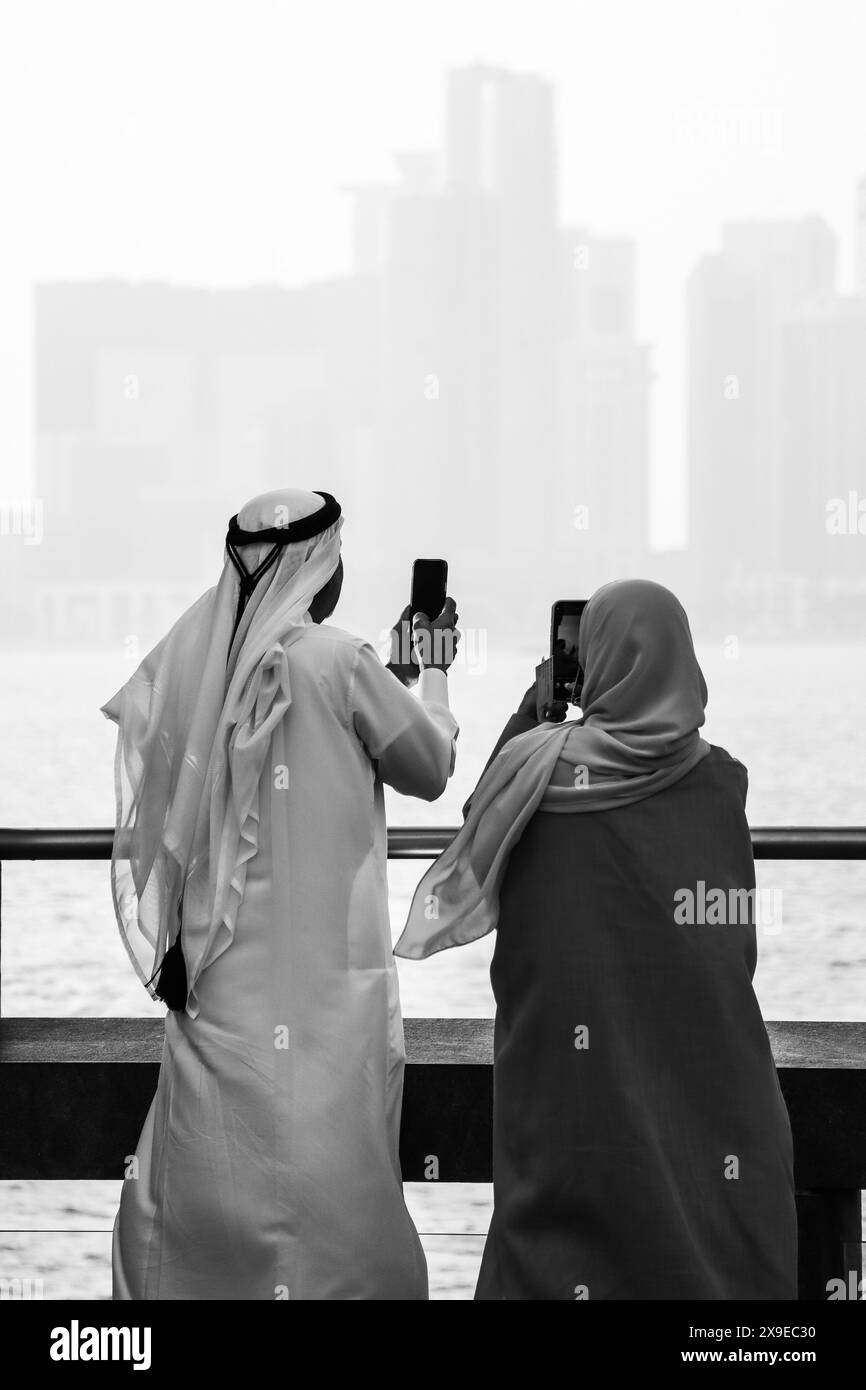 Una coppia che indossa abiti tradizionali del Qatar guarda lo skyline di Doha e scatta foto sul telefono. Foto Stock