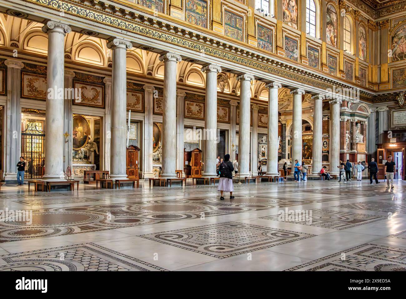 Persone che camminano davanti alle colonne ioniche di una delle navate laterali all'interno della Basilica di Santa Maria maggiore, una delle quattro Basiliche Papali a Roma, Italia Foto Stock