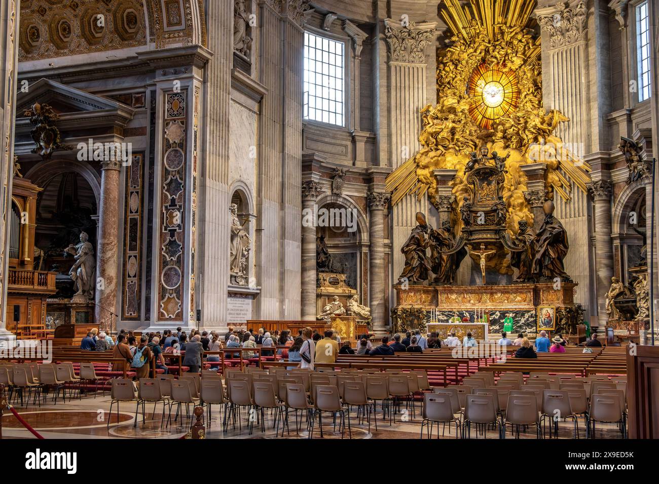 Le persone che partecipano a una messa Basilica di San Pietro di fronte alla Cattedra di San Pietro racchiusa in un involucro scolpito in bronzo dorato disegnato da Bernini. Foto Stock