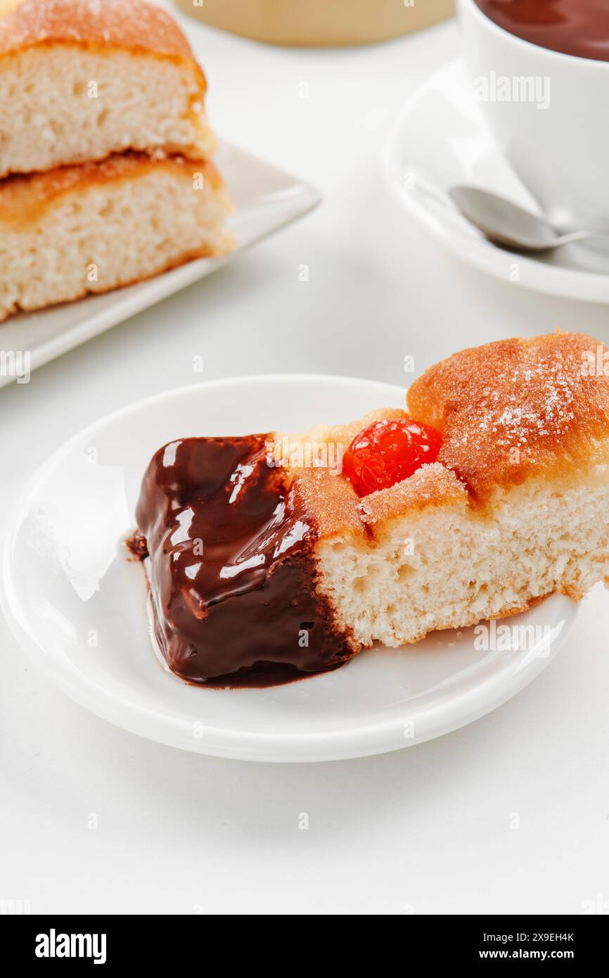 primo piano di un pezzo di coca catalana di sant joan, tipico della catalogna, spagna, immerso nella cioccolata calda, su una tavola bianca Foto Stock