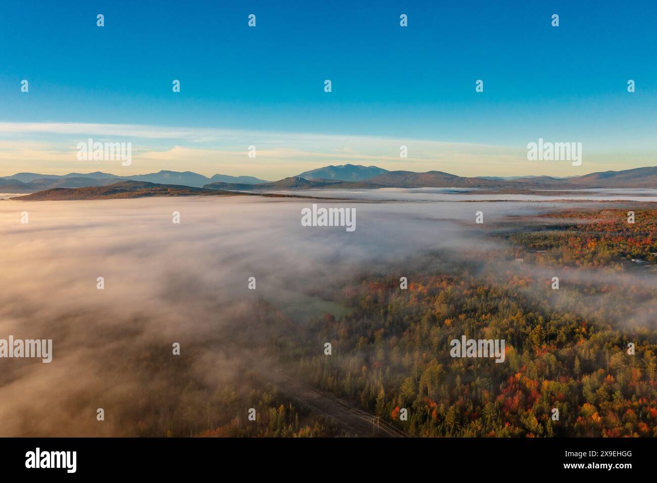 Vista dall'alto dei droni attraverso le nuvole su alberi multicolori nella nebbia all'alba in autunno. Sfondo delle montagne Foto Stock