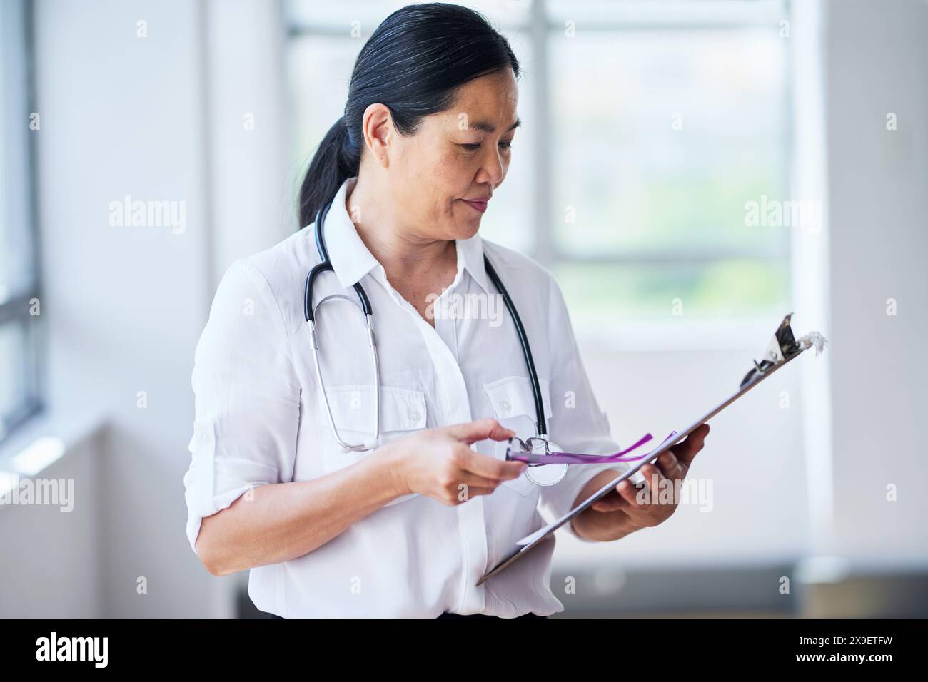 Donna asiatica Dottore che esamina la cartella paziente in Ufficio medico Foto Stock