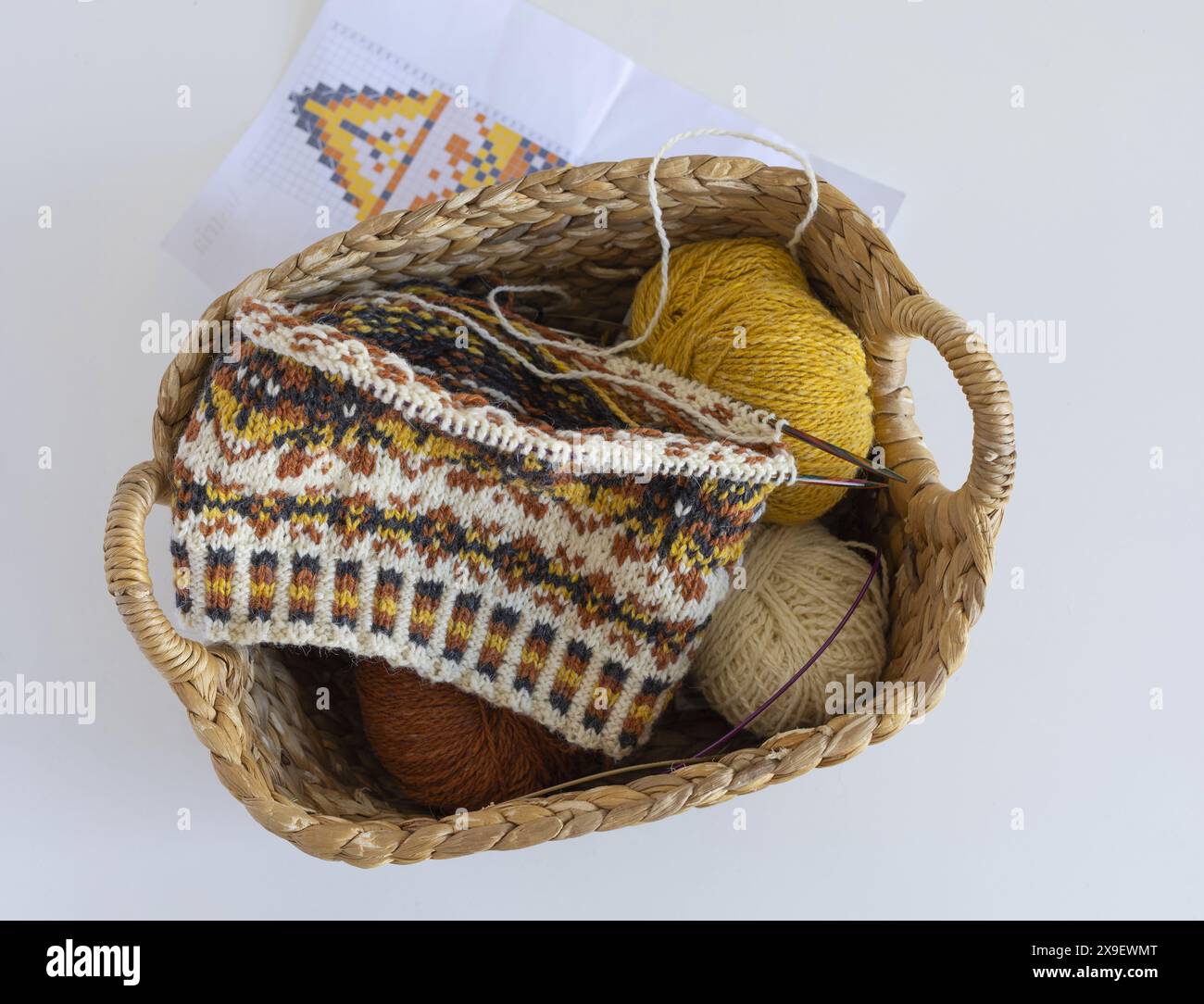 Direttamente sopra l'immagine del cappello lavorato a maglia di lana Fair Isle in corso sugli aghi con palle di filato e motivo a maglia in un cesto di vimini Foto Stock