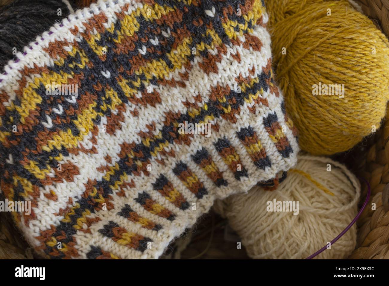 Foto ravvicinata del tradizionale cappello a maglia di lana di Fair Isle in corso sugli aghi con palle di filato Foto Stock