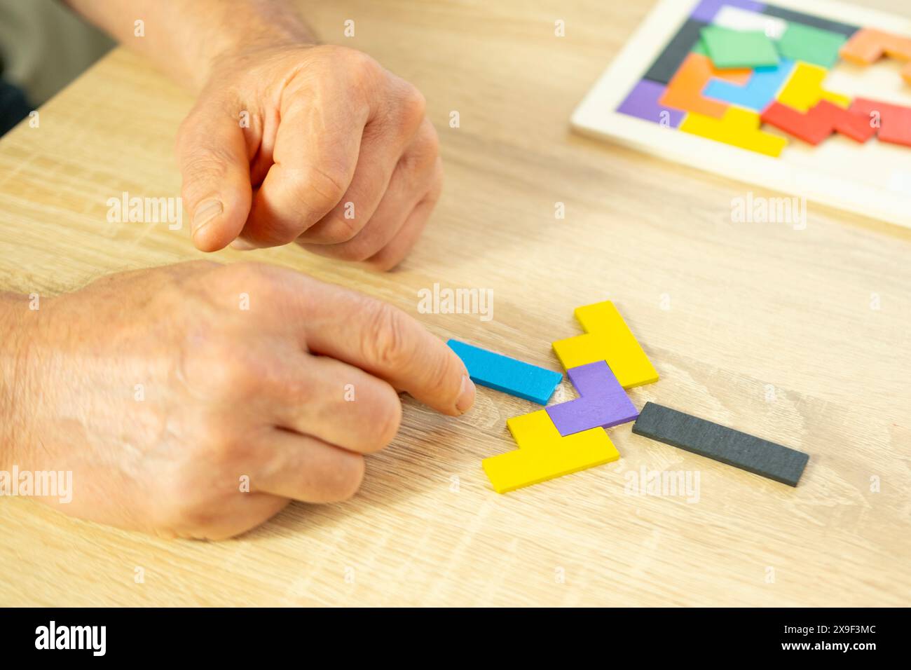 mano maschile manipola puzzle di legno colorato, vecchio anziano che compone forme geometriche, salute del cervello e benessere mentale, prevenire la demenza e. Foto Stock