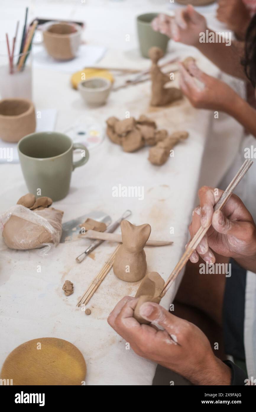 Mani ravvicinate di uno scultore maschio che forma una statuina di un gatto gattino di argilla Foto Stock