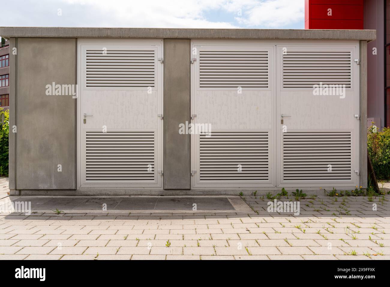 Moderno alloggiamento trasformatore con porte in alluminio bloccate. Ripresa diurna. Ombre sul marciapiede davanti. Foto Stock