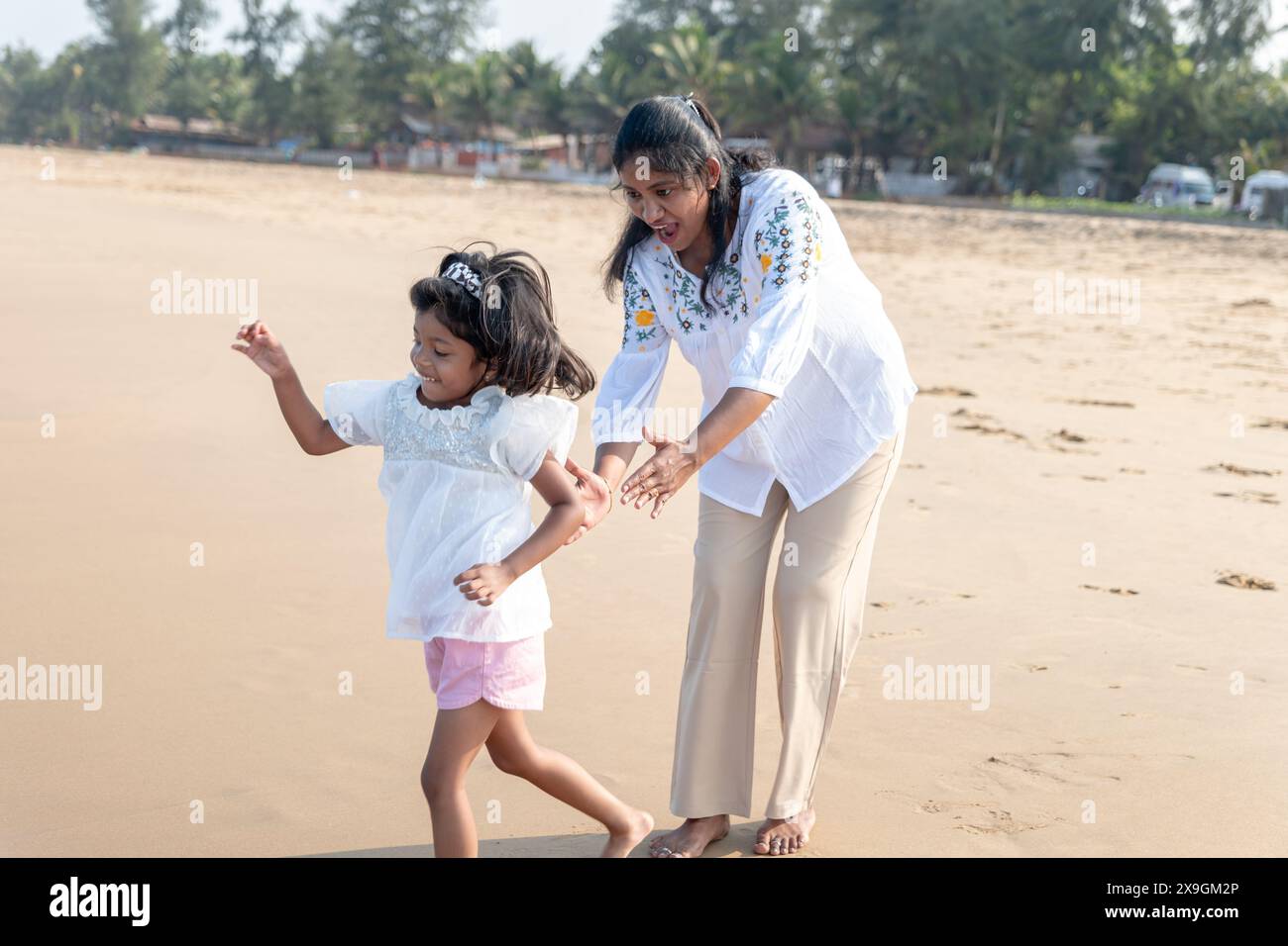 Un momento sereno in riva al mare: Una madre e sua figlia camminano mano nella mano sulla spiaggia baciata dal sole. Foto Stock