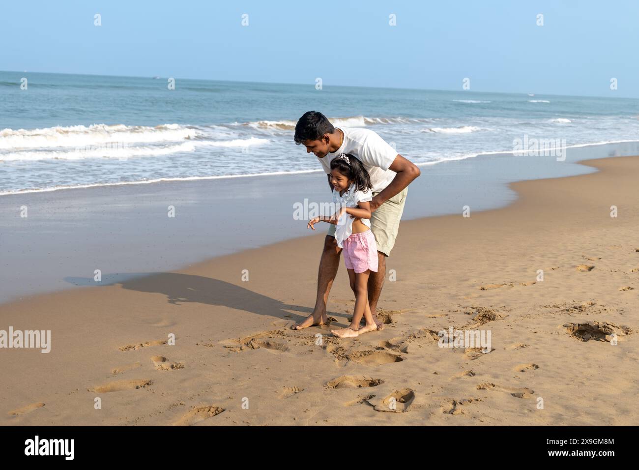 Padre e figlia creano ricordi giocando sulla sabbia su una spiaggia tranquilla. Foto Stock