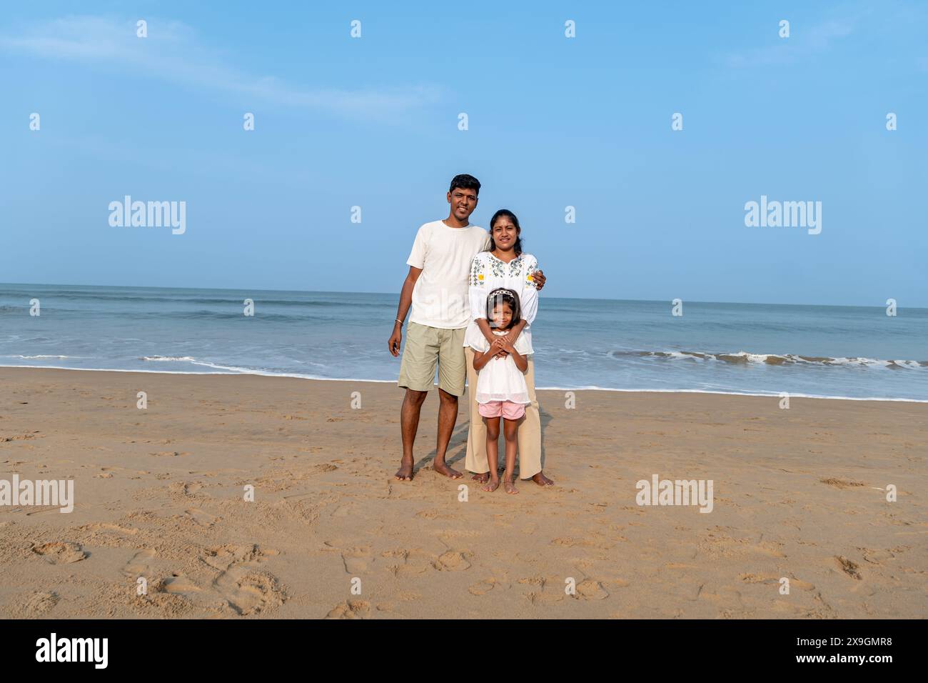 Una famiglia indiana affiatata sorge su una spiaggia sabbiosa, che guarda l'oceano. Momenti di amore e tranquillità. Foto Stock